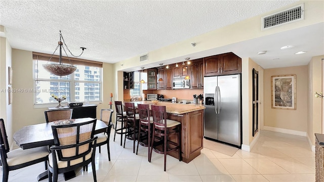 kitchen featuring appliances with stainless steel finishes, a textured ceiling, dark brown cabinets, light tile patterned floors, and pendant lighting