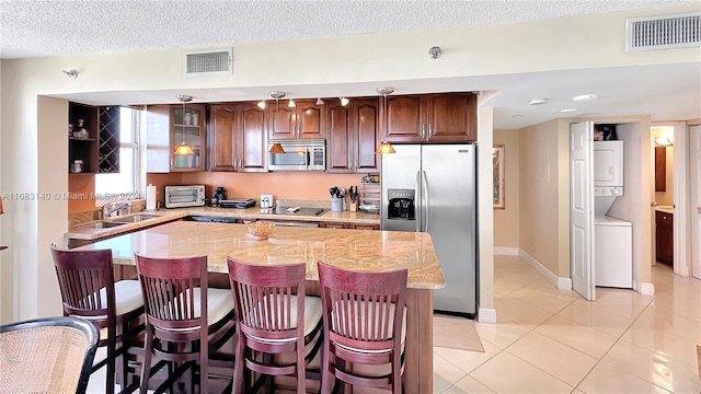 kitchen with stainless steel appliances, sink, light tile patterned floors, a breakfast bar, and stacked washer / drying machine