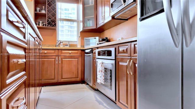 kitchen with appliances with stainless steel finishes, light tile patterned flooring, and light stone counters