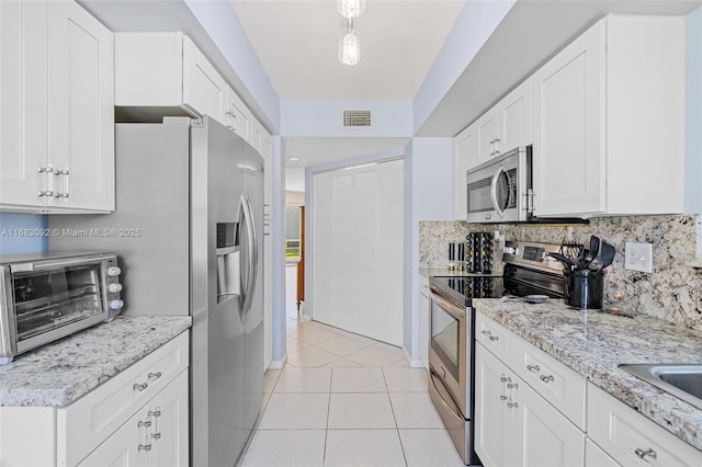 kitchen featuring light stone countertops, light tile patterned floors, tasteful backsplash, white cabinetry, and stainless steel appliances