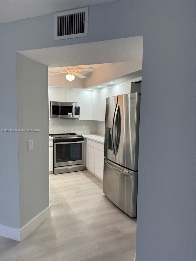 kitchen with appliances with stainless steel finishes, light hardwood / wood-style floors, white cabinetry, and ceiling fan