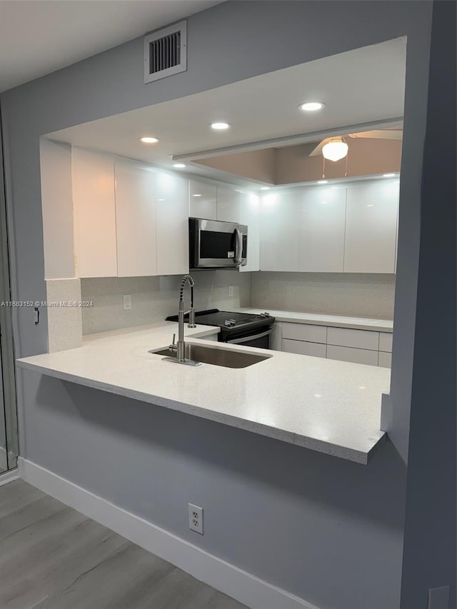 kitchen featuring white cabinetry, sink, kitchen peninsula, light hardwood / wood-style floors, and decorative backsplash