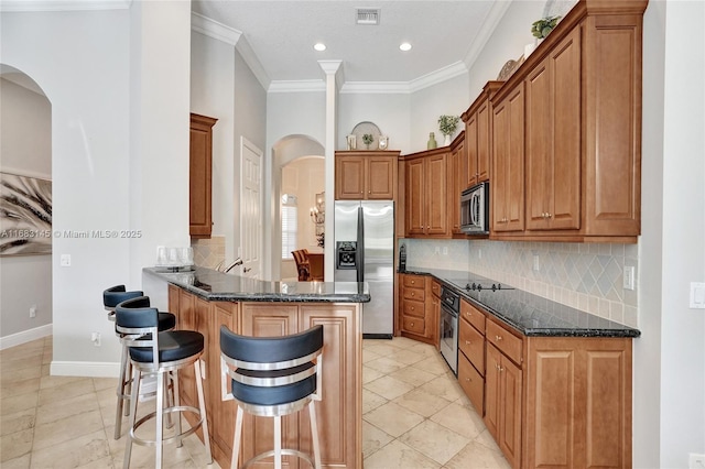 kitchen featuring crown molding, a breakfast bar, appliances with stainless steel finishes, dark stone countertops, and tasteful backsplash