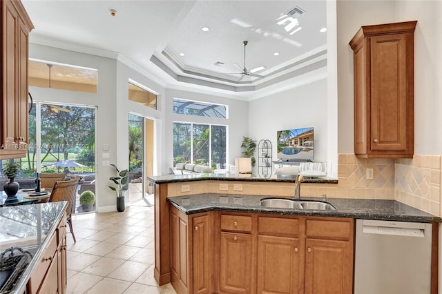 kitchen with sink, crown molding, stainless steel dishwasher, a raised ceiling, and dark stone counters