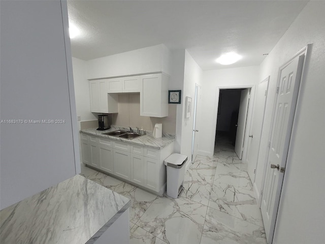 kitchen with white cabinets, sink, light stone counters, and a textured ceiling