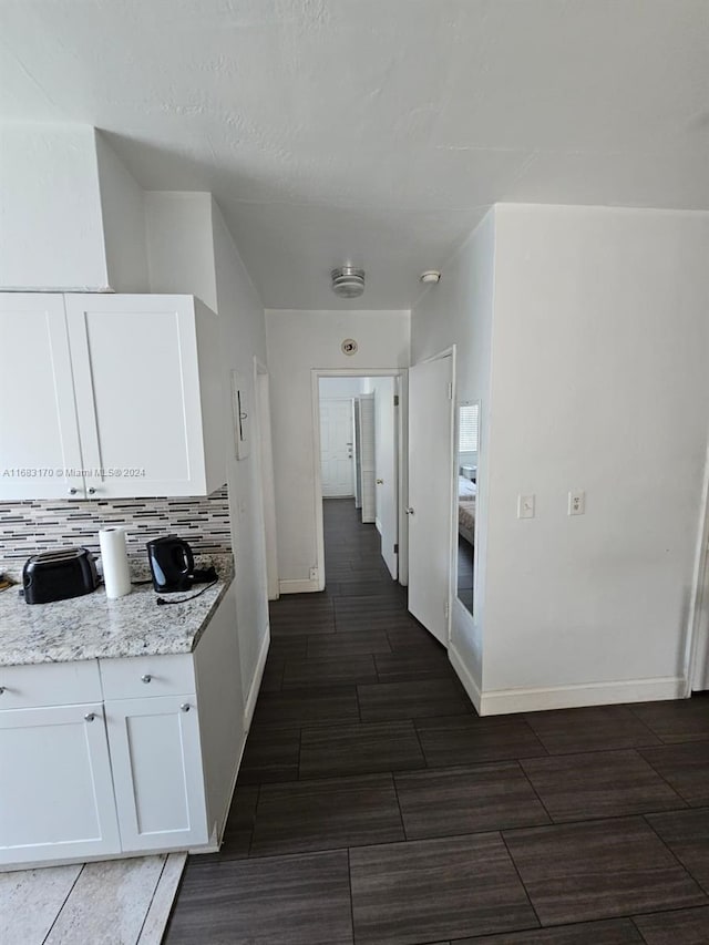 kitchen with light stone countertops, white cabinets, dark hardwood / wood-style flooring, and tasteful backsplash