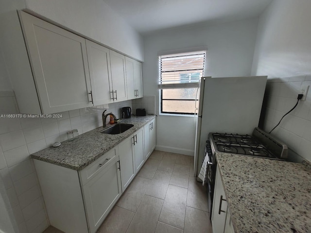 kitchen featuring gas range, sink, light stone countertops, tile walls, and white cabinets