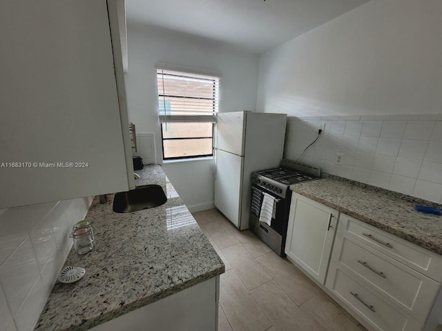 kitchen with light stone countertops, light tile patterned flooring, white refrigerator, stainless steel gas range oven, and white cabinets