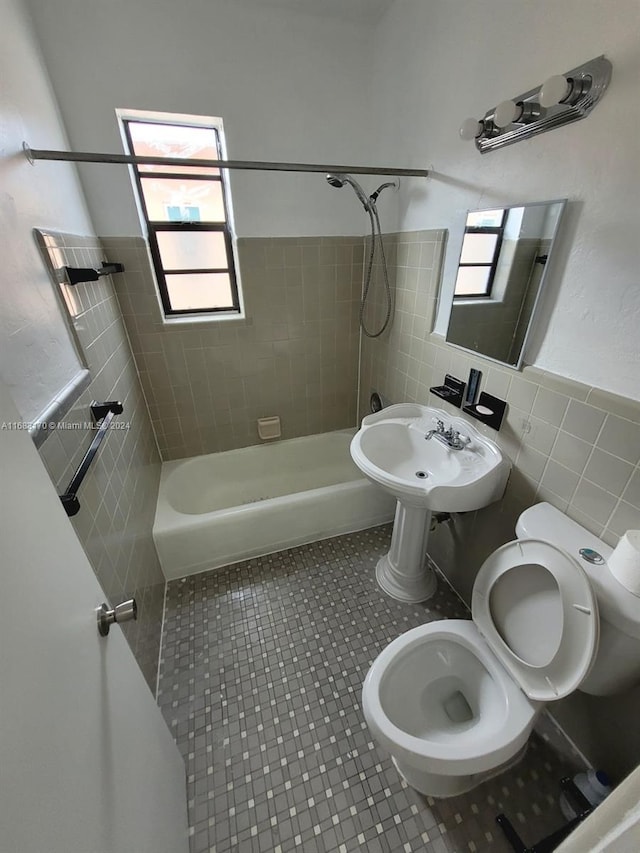 full bathroom featuring toilet, tiled shower / bath, sink, and tile walls