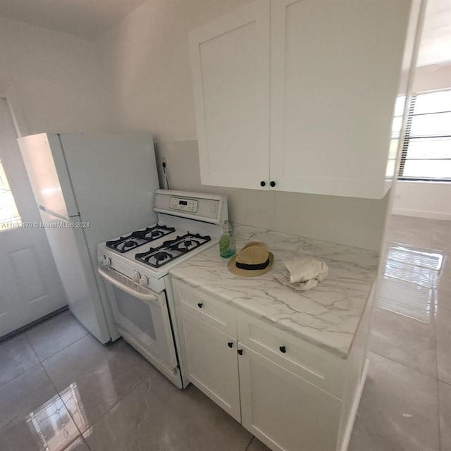 kitchen featuring white cabinets, light stone counters, white appliances, and light tile patterned floors