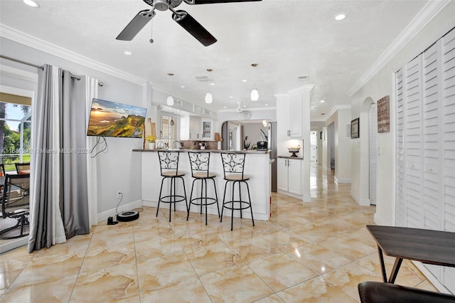 kitchen with hanging light fixtures, kitchen peninsula, crown molding, a kitchen bar, and white cabinets