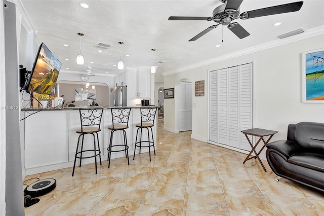 kitchen with kitchen peninsula, crown molding, pendant lighting, white cabinets, and stainless steel refrigerator