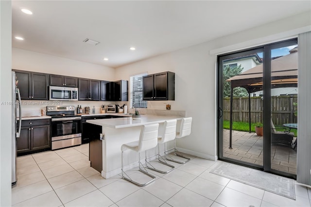 kitchen with light tile patterned flooring, kitchen peninsula, stainless steel appliances, and a breakfast bar area