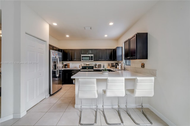 kitchen with kitchen peninsula, a kitchen breakfast bar, light tile patterned flooring, sink, and stainless steel appliances