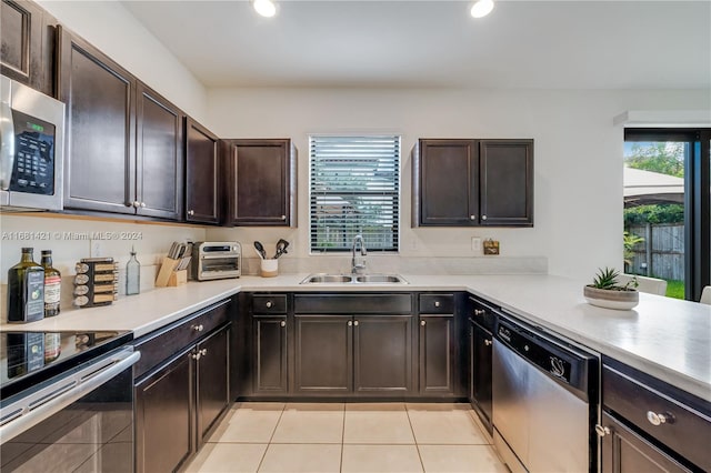 kitchen featuring dark brown cabinetry, light tile patterned flooring, appliances with stainless steel finishes, and sink