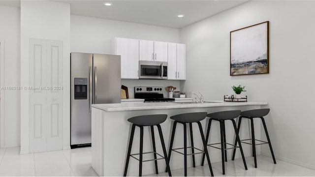 kitchen with kitchen peninsula, appliances with stainless steel finishes, a kitchen breakfast bar, white cabinetry, and sink