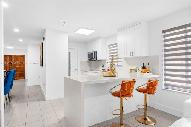 kitchen featuring kitchen peninsula, decorative backsplash, a breakfast bar area, light tile patterned flooring, and white cabinetry