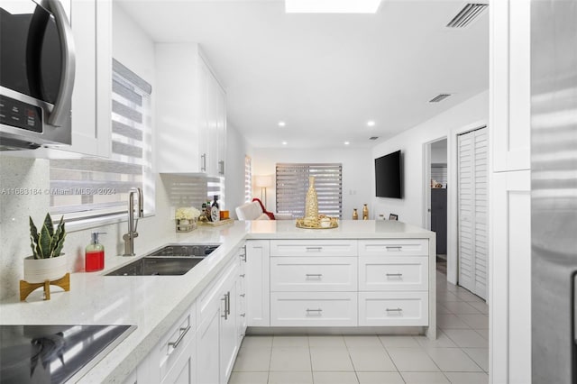 811 W 33rd St, Hialeah, FL 33012 - kitchen with stainless steel microwave, light tile patterned floors, a peninsula, black electric stovetop, and white cabinets