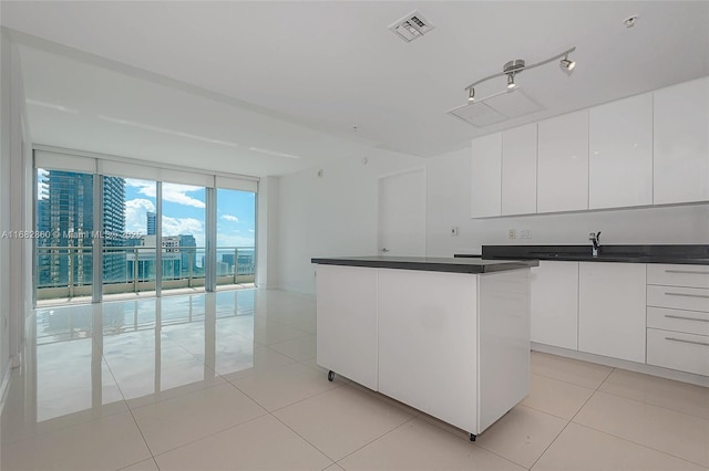 kitchen with floor to ceiling windows, sink, a kitchen island, light tile patterned flooring, and white cabinets