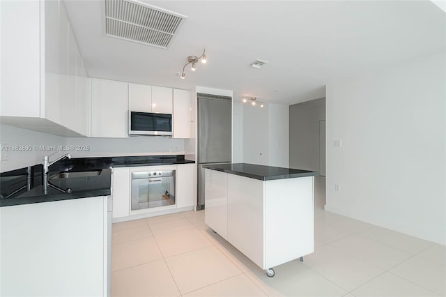 kitchen featuring sink, stainless steel appliances, a kitchen island, white cabinets, and light tile patterned flooring