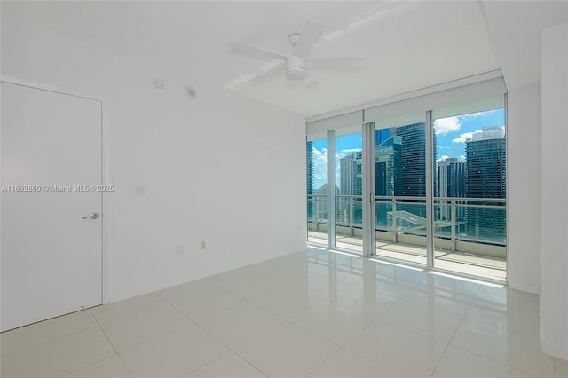 tiled spare room featuring expansive windows and ceiling fan