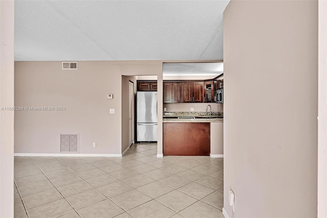 kitchen with a textured ceiling, dark brown cabinets, light tile patterned floors, and stainless steel appliances