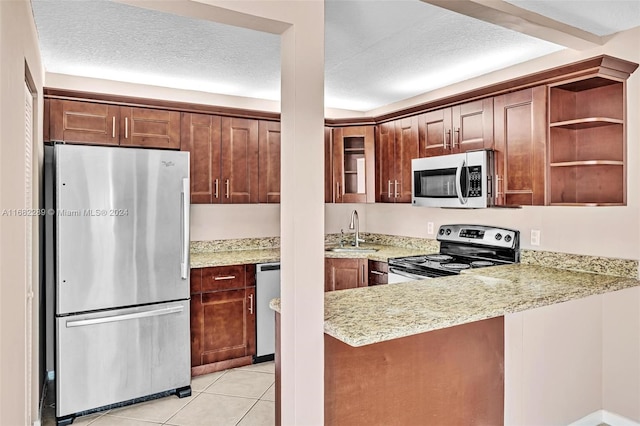 kitchen featuring kitchen peninsula, light stone counters, a textured ceiling, stainless steel appliances, and sink