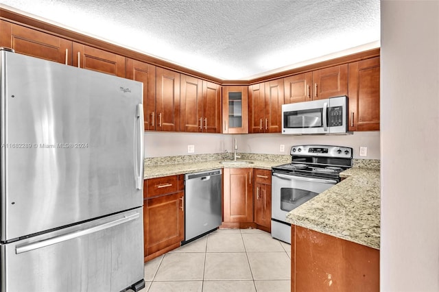 kitchen with light stone countertops, sink, a textured ceiling, light tile patterned floors, and appliances with stainless steel finishes