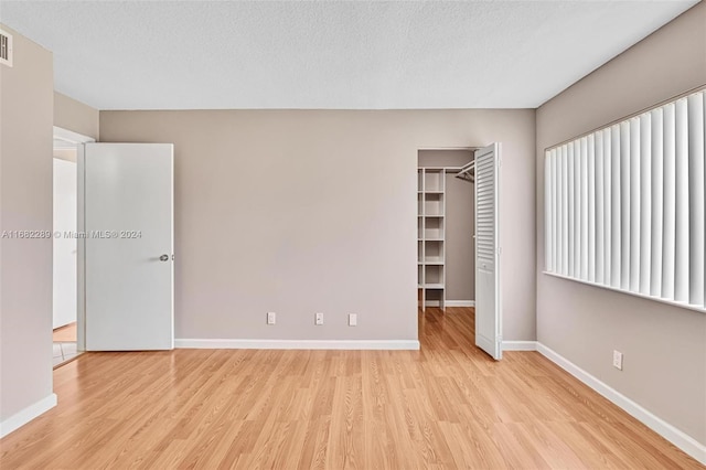 unfurnished bedroom with a spacious closet, a closet, light hardwood / wood-style floors, and a textured ceiling