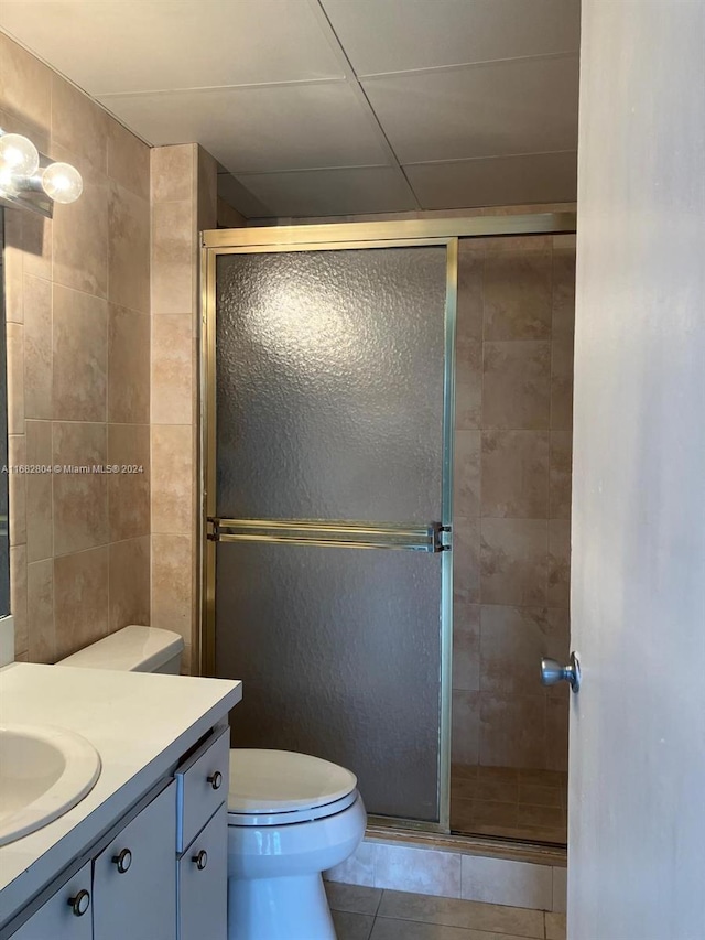 bathroom with tile walls, toilet, a shower with shower door, vanity, and tile patterned floors