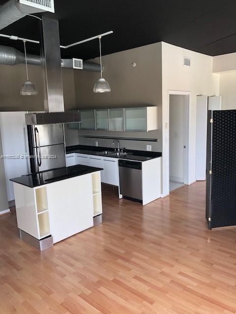 kitchen with hanging light fixtures, stainless steel appliances, sink, light wood-type flooring, and white cabinetry