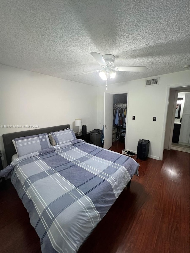 bedroom with a walk in closet, a textured ceiling, dark hardwood / wood-style flooring, a closet, and ceiling fan