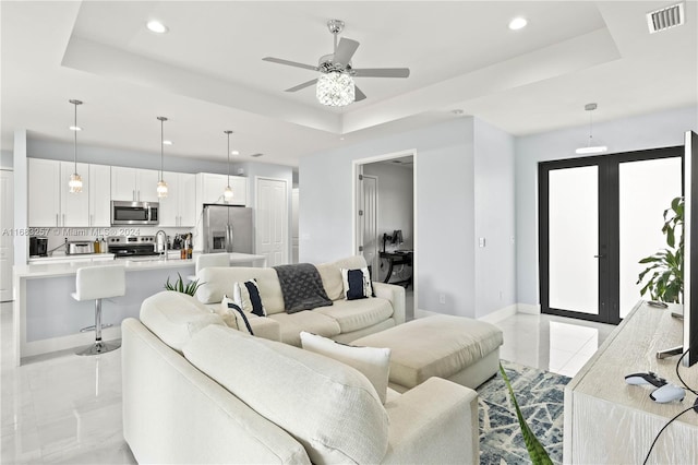 living room with ceiling fan, a raised ceiling, and french doors