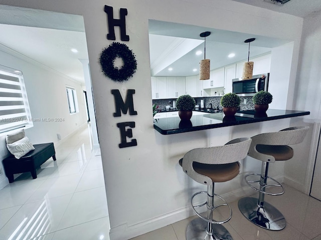 kitchen featuring white cabinets, decorative backsplash, hanging light fixtures, a breakfast bar area, and light tile patterned flooring