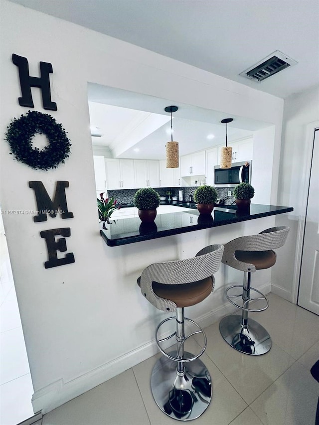 kitchen featuring white cabinetry, decorative light fixtures, backsplash, and a breakfast bar