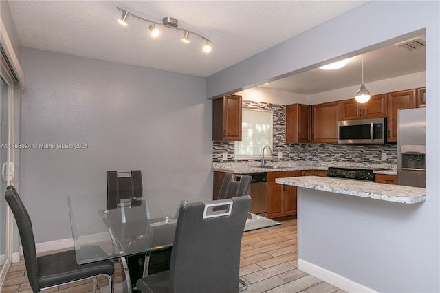 2510 SW Natura Blvd, Deerfield Beach, FL 33441 - kitchen featuring stainless steel appliances, backsplash, light wood-type flooring, brown cabinets, and a textured ceiling