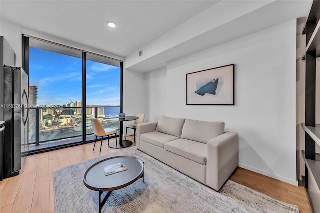 living room featuring light wood-type flooring, a wall of windows, and a water view