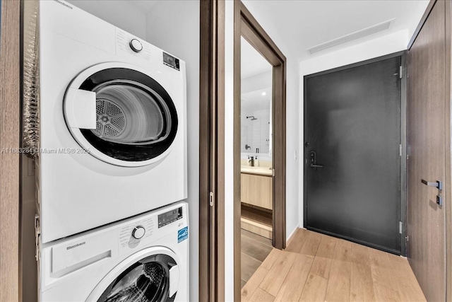 clothes washing area with stacked washing maching and dryer and light wood-type flooring