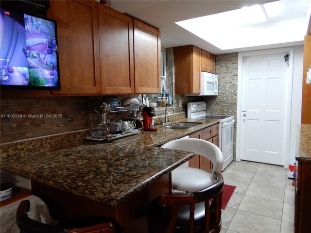 kitchen with backsplash, white appliances, a breakfast bar area, and dark stone counters