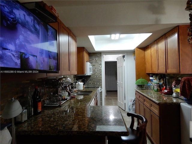 kitchen with kitchen peninsula, tasteful backsplash, dark stone counters, light tile patterned floors, and stainless steel electric range oven