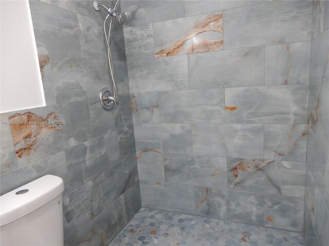 bathroom with toilet, tiled shower, and tile walls