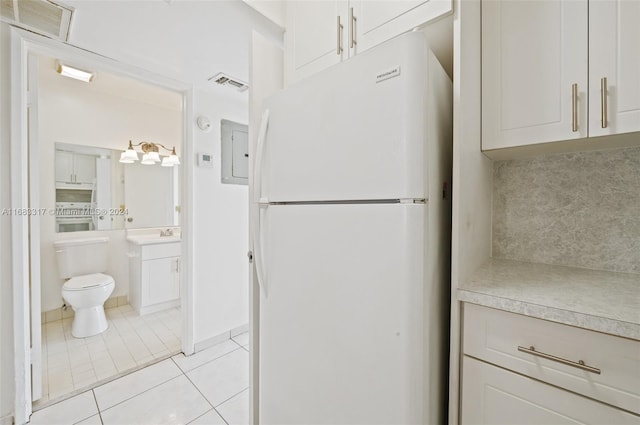 kitchen featuring stainless steel range oven, light tile patterned floors, white refrigerator, and white cabinets