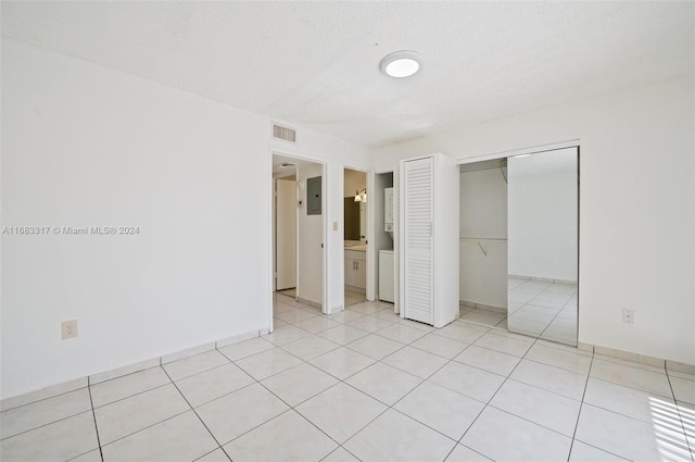 unfurnished bedroom with a closet, a textured ceiling, ensuite bathroom, and light tile patterned floors