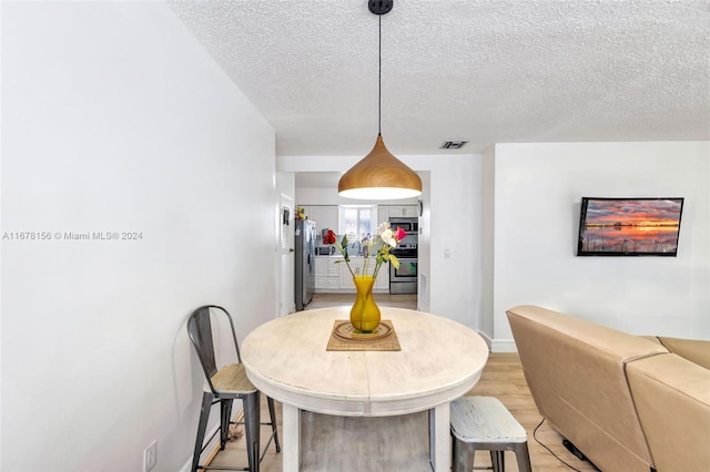 dining room with light wood-type flooring and a textured ceiling