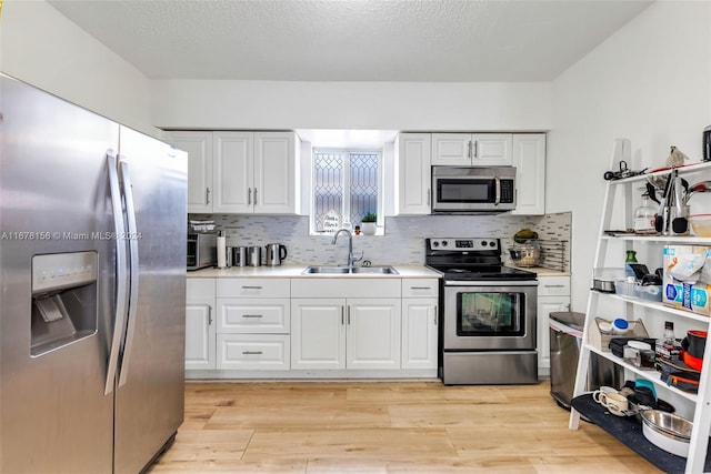 kitchen featuring sink, light hardwood / wood-style flooring, tasteful backsplash, white cabinetry, and stainless steel appliances