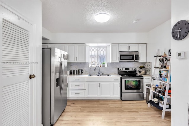 kitchen featuring white cabinetry, sink, tasteful backsplash, light hardwood / wood-style floors, and appliances with stainless steel finishes