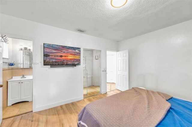 bedroom featuring hardwood / wood-style flooring, a textured ceiling, and ensuite bath