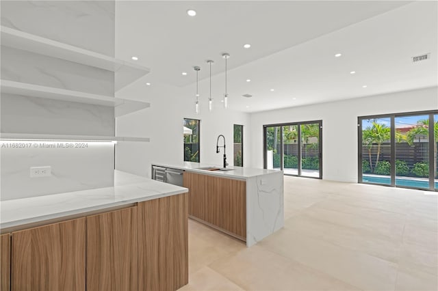 kitchen with light tile patterned floors, light stone countertops, a kitchen island with sink, sink, and decorative light fixtures