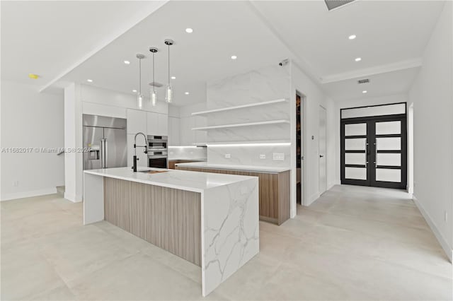 kitchen featuring stainless steel appliances, a large island, light stone countertops, pendant lighting, and white cabinetry