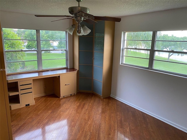 unfurnished office with light wood-type flooring, a textured ceiling, built in desk, and ceiling fan